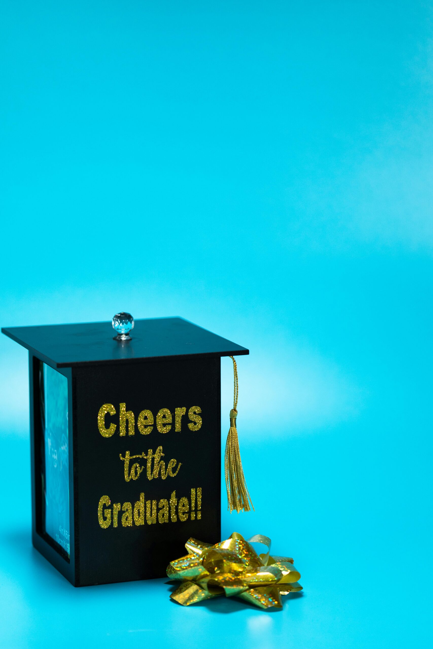 A decorative graduation gift box styled as a cap with tassel against a bright blue background.